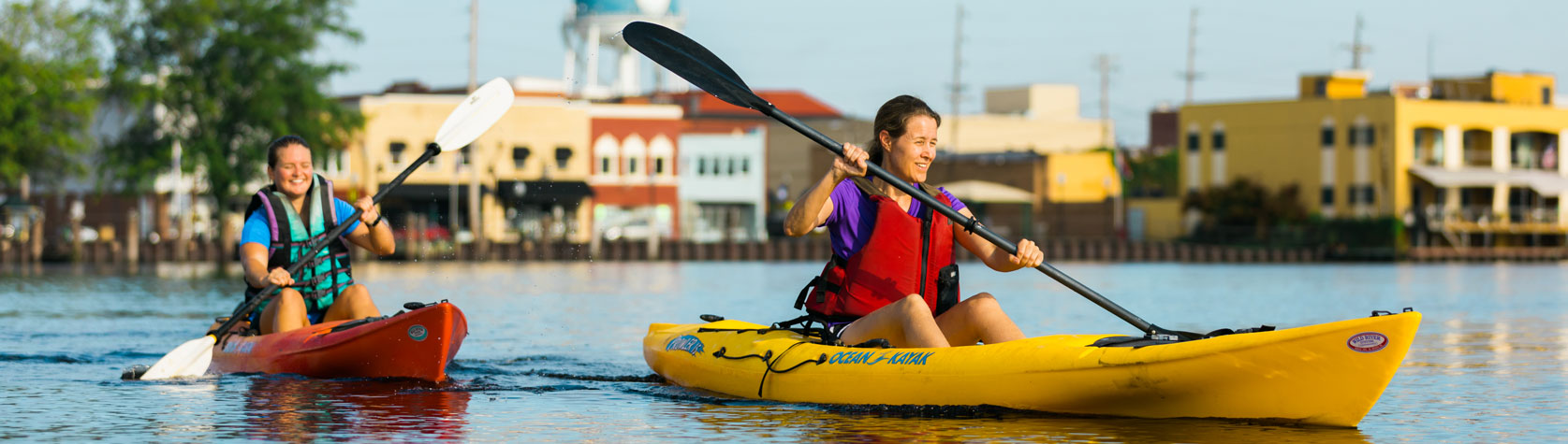 women kayaking on downtown waterfront river with buildings in background